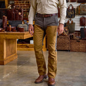 A man in a tan shirt and Tom Beckbe Burwell Brush Pant stands indoors near leather bags and wood furniture.