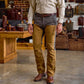 A man in a tan shirt and Tom Beckbe Burwell Brush Pant stands indoors near leather bags and wood furniture.