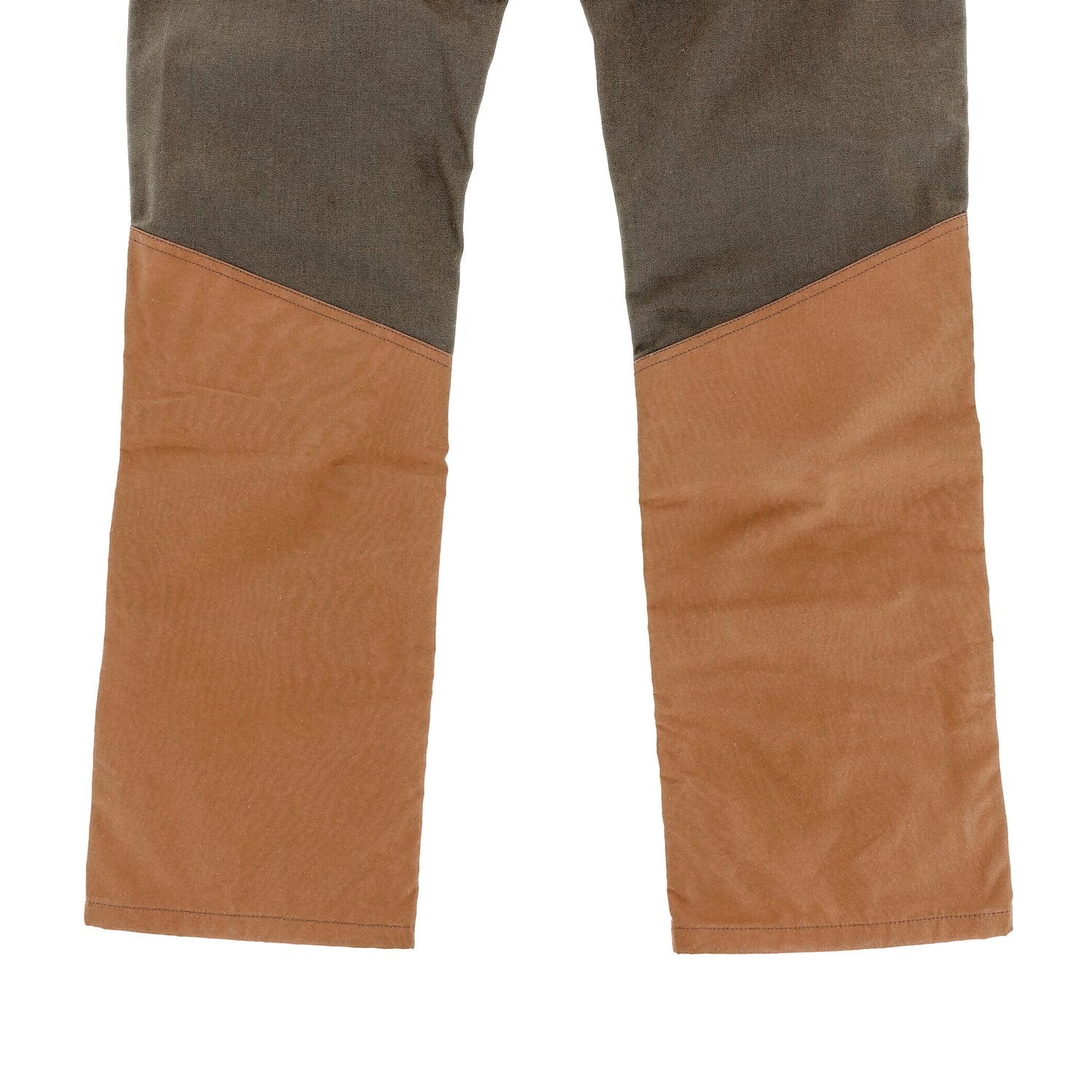 A close-up of Tom Beckbe's Burwell Brush Pant features brown fabric below the knees and dark gray above with a diagonal seam.