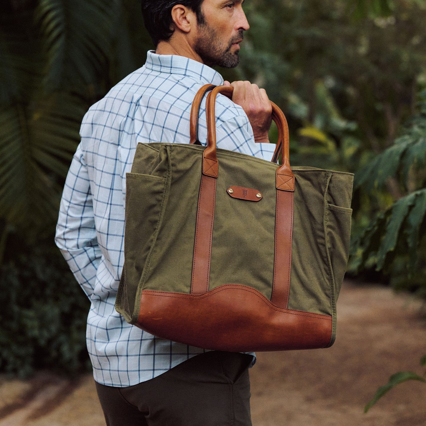 A man in a checkered shirt carries the Tom Beckbe Canvas Carryall Bag outdoors.