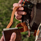 Man holds leather wallet before storing inside an interior mesh zipper pocket on a Fly Fishing Vest.