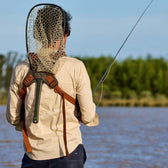 Back view of a fisherman wearing a fly fishing vest with a fishing net attached to the back yoke.