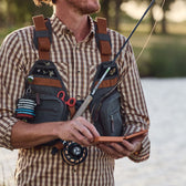 Man wears a Tom Beckbe all-weather fly fishing vest loaded with gear while holding a fishing rod.
