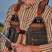 Man wears an all-weather fly fishing vest holding red scissors and flies while holding a fishing rod.