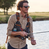 Man fishing on a stream with a fly rod while wearing an all-weather fly fishing vest holding flies.