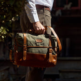A person outdoors with a Tom Beckbe Messenger Bag, wearing a striped shirt and brown pants.
