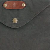 Close-up of a Tom Beckbe Canvas Portfolio, gray with leather and metal button closure, plus an embossed leather patch.