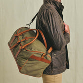A person carries the Tom Beckbe Canvas Weekender Duffel Bag over their shoulder.