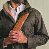 A man in a dark jacket holds a Tom Beckbe Canvas Weekender Duffel Bag strap across his chest over a checked shirt.