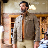 A man indoors wears a Tom Beckbe Chatom Jacket over an orange shirt and khaki pants.
