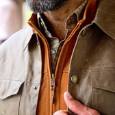 A man unzips the durable Tom Beckbe Chatom Jacket over an orange zip-up and plaid shirt.