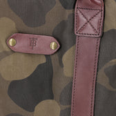 Close-up of the Tom Beckbe Classic Camo Carryall Bag with waxed canvas, leather strap, and embossed patch with brass studs.
