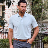Man in a Tom Beckbe Coastal Polo Shirt and gray pants strolls near a brick building and lush greenery.