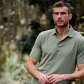 A man outdoors wears a classic Tom Beckbe Coastal Polo Shirt in green, standing against a blurred natural backdrop.