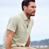 A man in a Tom Beckbe Coastal Polo Shirt sits outdoors, gazing neutrally into the distance against a blurred sky.