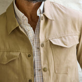 A man wears a Tom Beckbe Crawford Jacket in beige over a white plaid button-up shirt, shown from shoulders to chest.