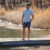 Man on a wooden dock by a lake, wearing a checkered shirt and Crenshaw Performance Short from Tom Beckbe.