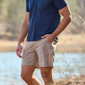 Man in a navy tee and Tom Beckbe Crenshaw Performance Short by a lake, one hand in his pocket.