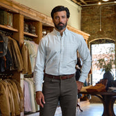 A man in a Tom Beckbe Culver Oxford Shirt and brown pants stands in a store with racks of jackets and shirts.