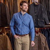 Man wearing the Tom Beckbe Culver Oxford Shirt stands in a clothing store with jackets hanging behind him.