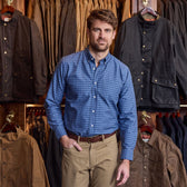 A man wearing the Tom Beckbe Culver Oxford Shirt stands in front of jackets in a clothing store.