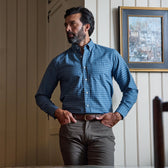 Man wears the Culver Oxford Shirt by Tom Beckbe with brown pants, standing indoors near a framed painting.