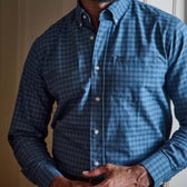 Man wearing Tom Beckbes Culver Oxford Shirt in blue checks, standing indoors with hands folded at the waist.