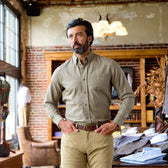 A man in a Tom Beckbe Culver Oxford Shirt and khaki pants stands in a store with brick walls and wooden shelves.