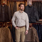 A man in a Tom Beckbe Culver Oxford Shirt and khaki pants stands before racks of jackets in a clothing store.