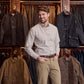 Man in a Tom Beckbe Culver Oxford Shirt stands before a display of jackets in a clothing store.
