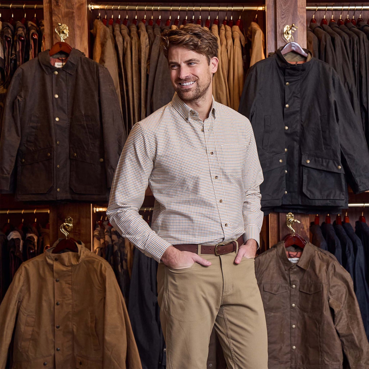 Man in a Tom Beckbe Culver Oxford Shirt stands before a display of jackets in a clothing store.