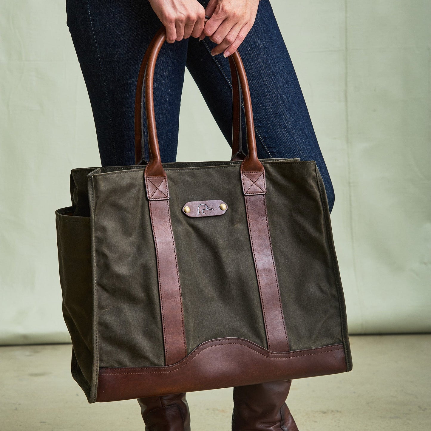 Person holding the Tom Beckbe DU Canvas Carryall, a large olive green tote with brown leather handles.