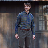 Man wears Tom Beckbe Dixon Brushed Cotton Twill Shirt with olive pants outside a dark wooden building.