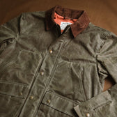 The Tom Beckbe Womens Steward Jacket in olive green features a waxed shell, corduroy collar, brass snaps, and front pockets.