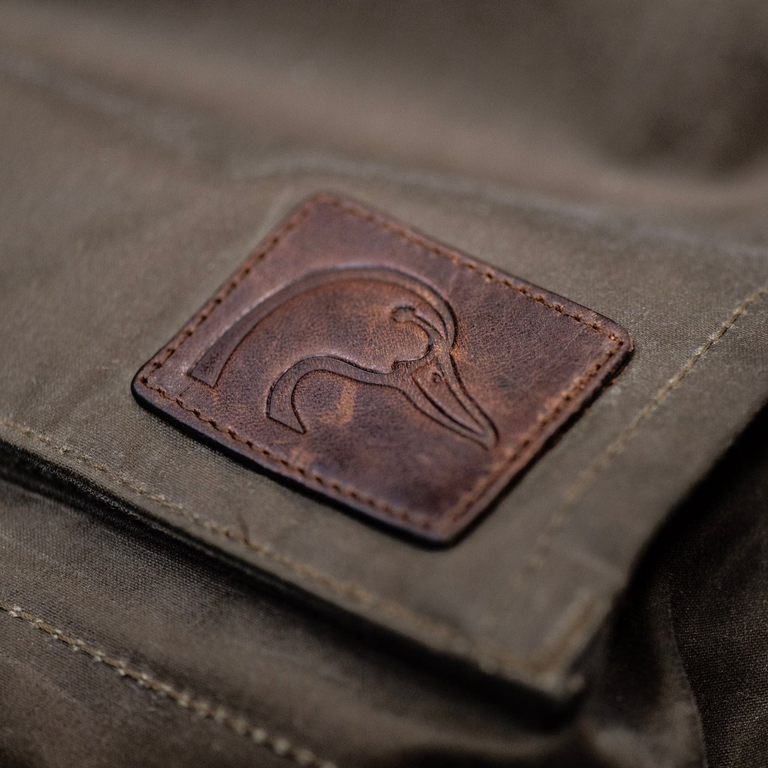 A brown leather patch with a duck logo accents the Womens Steward Jacket by Tom Beckbe in waxed shelter cloth.