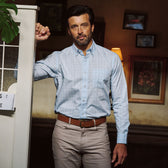 Man with dark hair and beard wears a Tom Beckbe Ensley Pinpoint Oxford Shirt in light blue, standing by a white cabinet.
