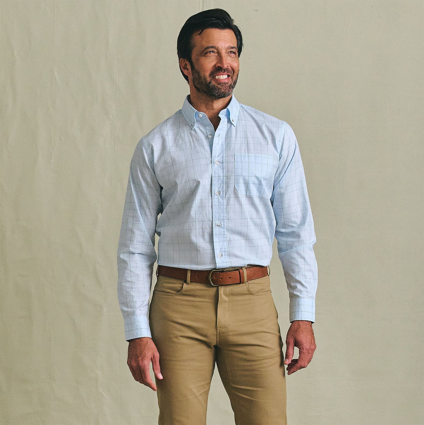 Man wearing a Tom Beckbe Ensley Pinpoint Oxford Shirt in light blue, khaki pants, and a brown belt against a plain background.