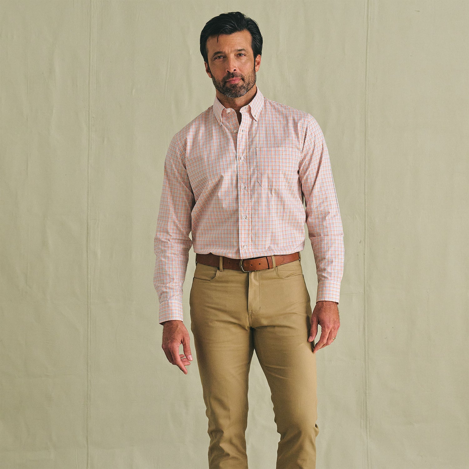 Man in Tom Beckbe Ensley Pinpoint Oxford Shirt, tucked into tan pants with brown belt, against a beige background.