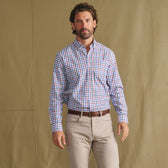 Man in Tom Beckbe Ensley Pinpoint Oxford Shirt and beige pants poses before a plain tan backdrop.