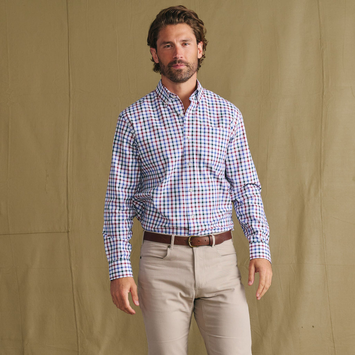 Man in Tom Beckbe Ensley Pinpoint Oxford Shirt and beige pants poses before a plain tan backdrop.