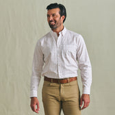Man in a Tom Beckbe Ensley Pinpoint Oxford Shirt and khaki pants stands against a plain background, looking to the side.