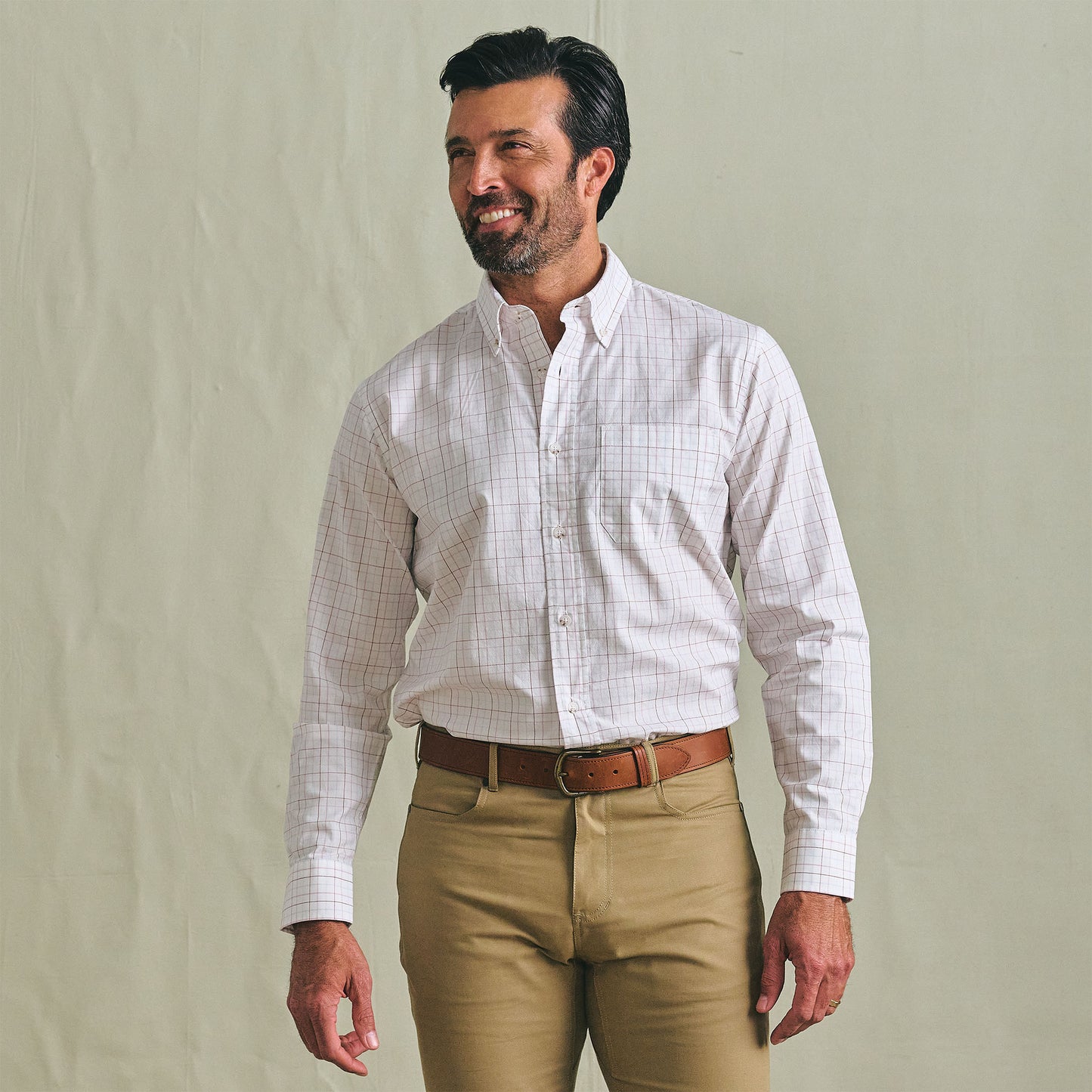Man in a Tom Beckbe Ensley Pinpoint Oxford Shirt and khaki pants stands against a plain background, looking to the side.