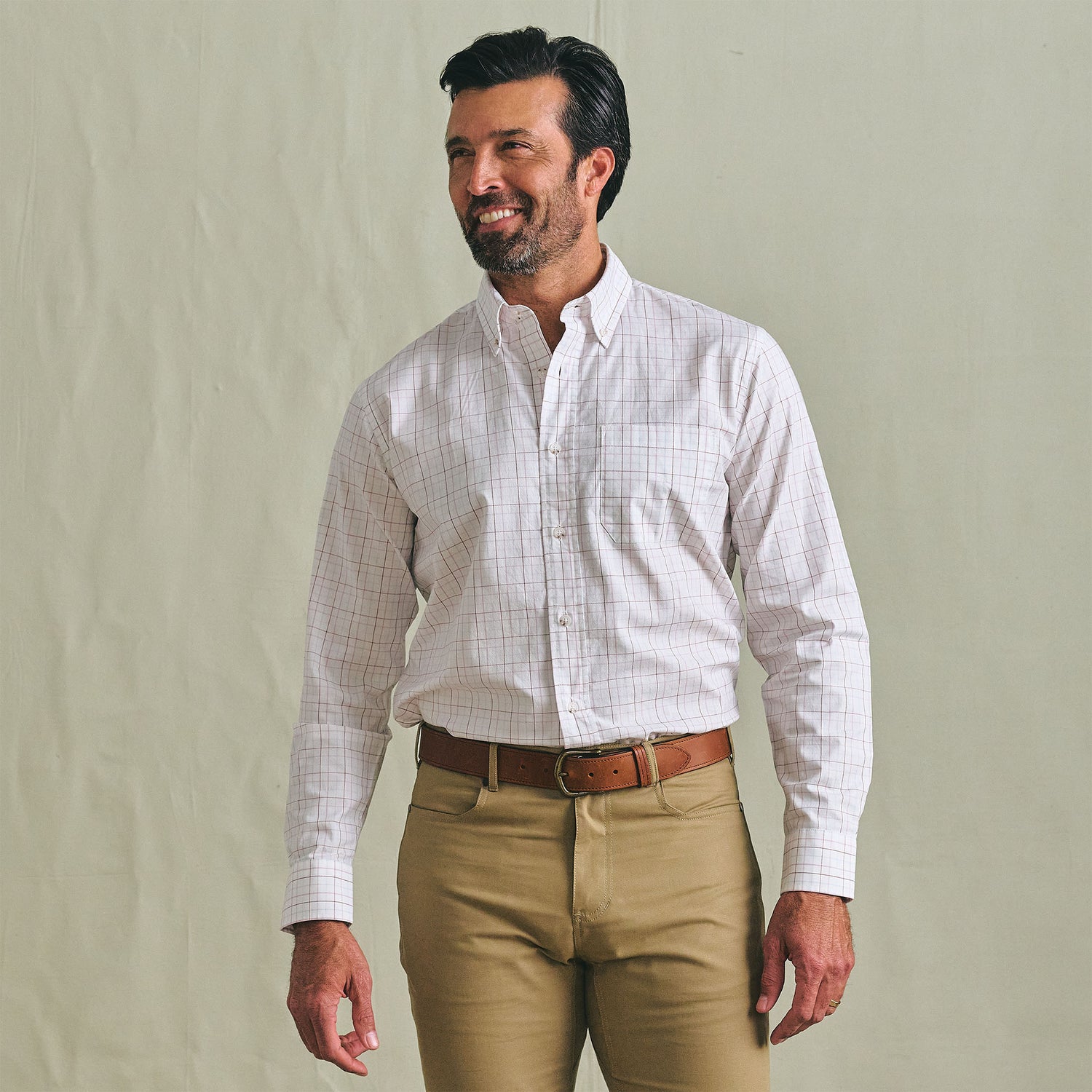 Man in a Tom Beckbe Ensley Pinpoint Oxford Shirt and khaki pants stands against a plain background, looking to the side.