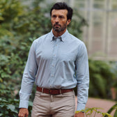 A man with dark hair and a beard wears the Tom Beckbe Ensley Pinpoint Oxford Shirt, standing outdoors in greenery.