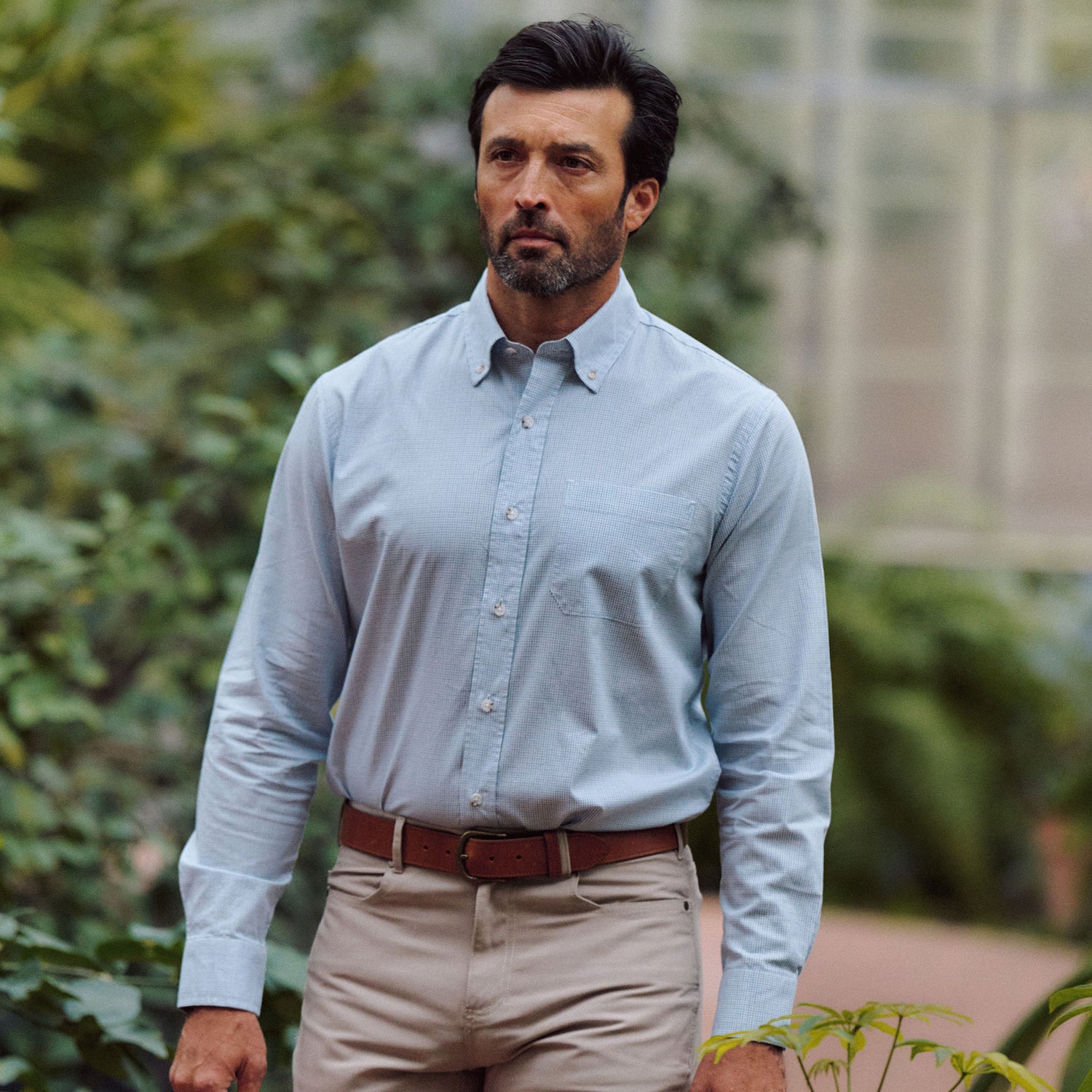A man with dark hair and a beard wears the Tom Beckbe Ensley Pinpoint Oxford Shirt, standing outdoors in greenery.
