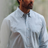 Man wearing the Tom Beckbe Ensley Pinpoint Oxford Shirt in light blue, standing indoors with a blurred background.