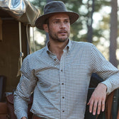 Man in a Tom Beckbe Field Hat leans against an outdoor vehicle, surrounded by trees in a natural setting.