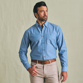 Man wears the Tom Beckbe Hanover Chambray Shirt and beige pants, standing against a plain light background, looking aside.
