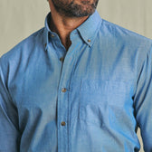 Man wearing the Tom Beckbe Hanover Chambray Shirt in light blue, shown shoulders up with front pocket detail.