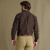 Man faces away in Tom Beckbe Hartwell Moleskin Shirt and tan pants before heritage waterfowl apparel backdrop.